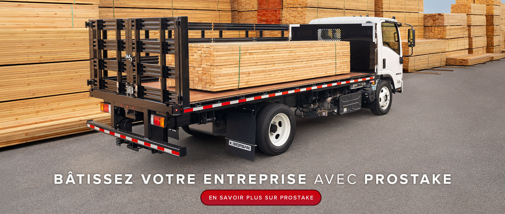 Un camion à plateau blanc avec des ridelles noires est garé, chargé de bois, entouré de piles de bois dans un grand chantier de bois d'œuvre.